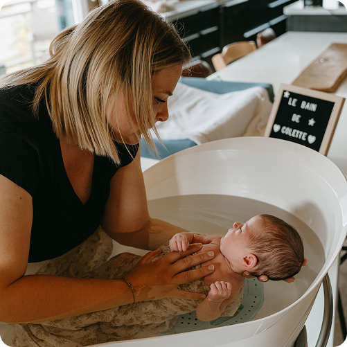 Julie avec un bébé dans les mains dans un bain pour bébé