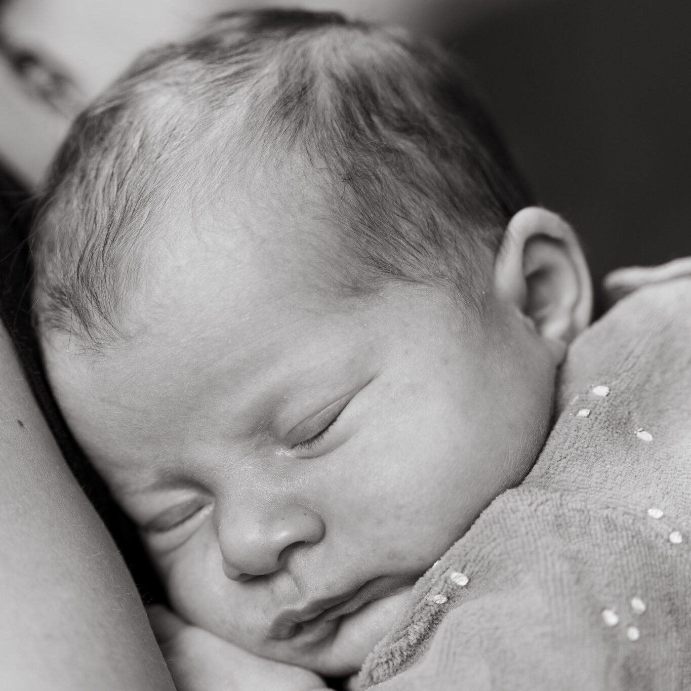 Image en noir et blanc d'un bébé qui dort dans les bras de sa maman